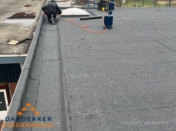 Dakdekker repareert bitumen dakbedekking op groot plat dak in Stadskanaal